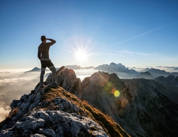 Climber standing on the mountain peak and watching the sun